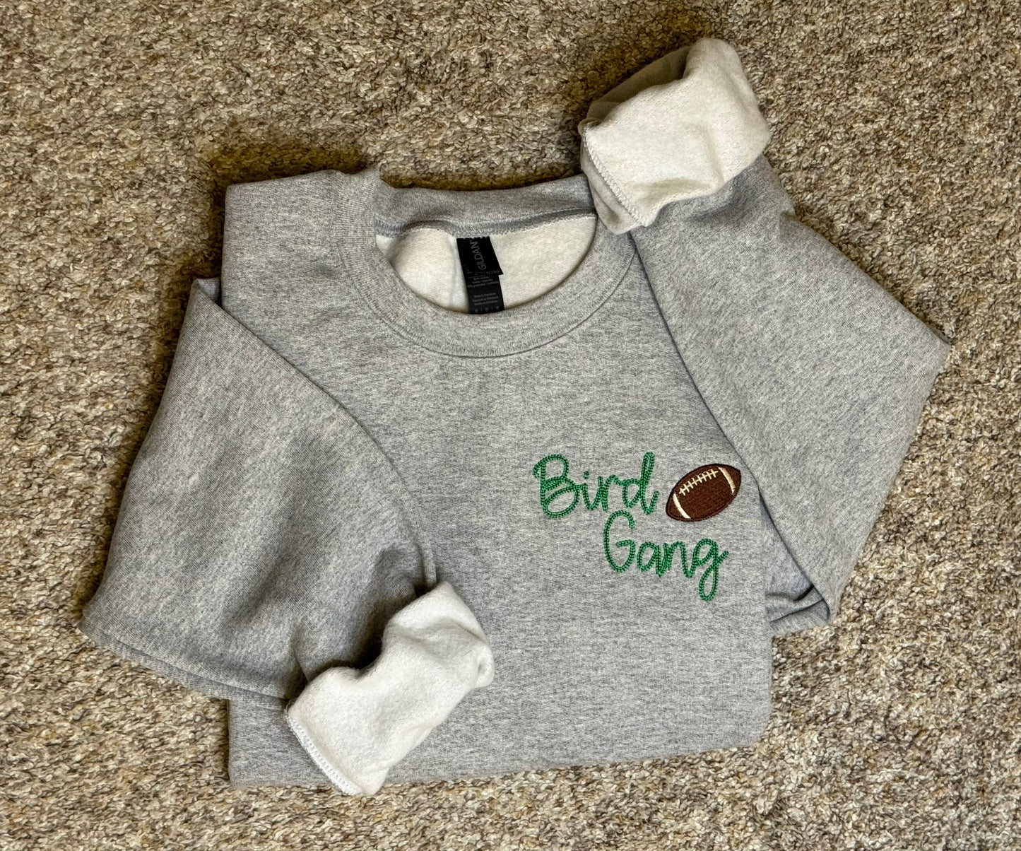 Gray sweatshirt with 'Bird Gang' embroidered text and football graphic on a beige background