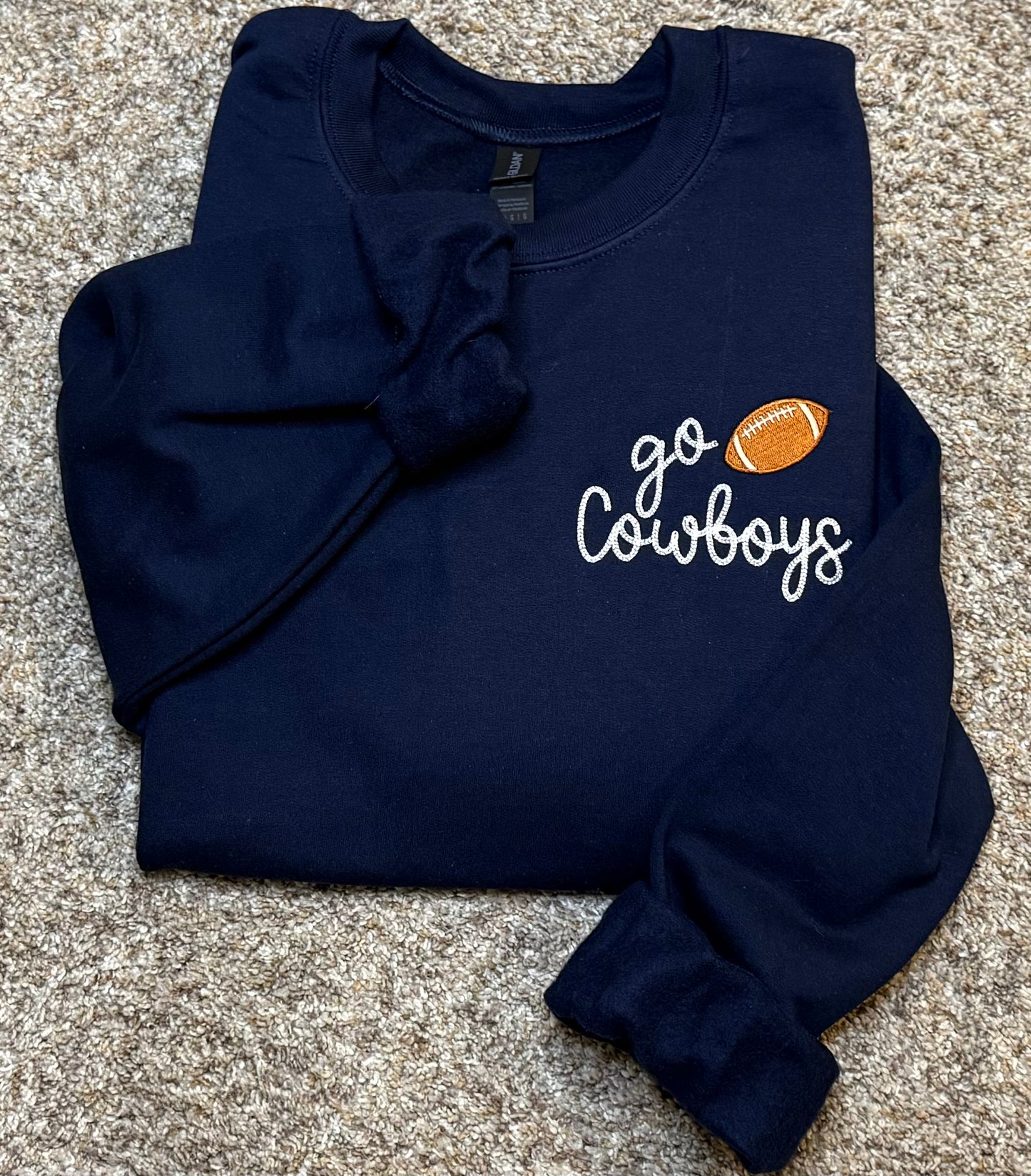 Navy blue sweatshirt with 'go Cowboys' embroidered text and football graphic on a beige background