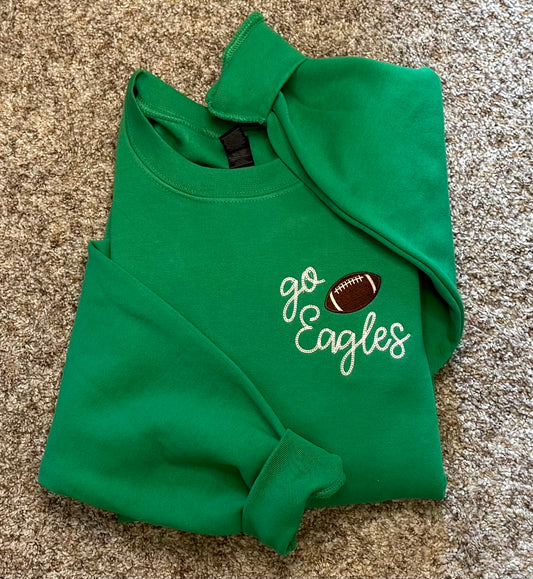 Green sweatshirt with 'go Eagles' embroidered text and football graphic on a beige background