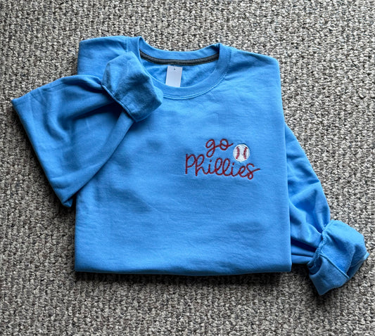 Folded blue sweatshirt with 'go Phillies' embroidered text on a gray background