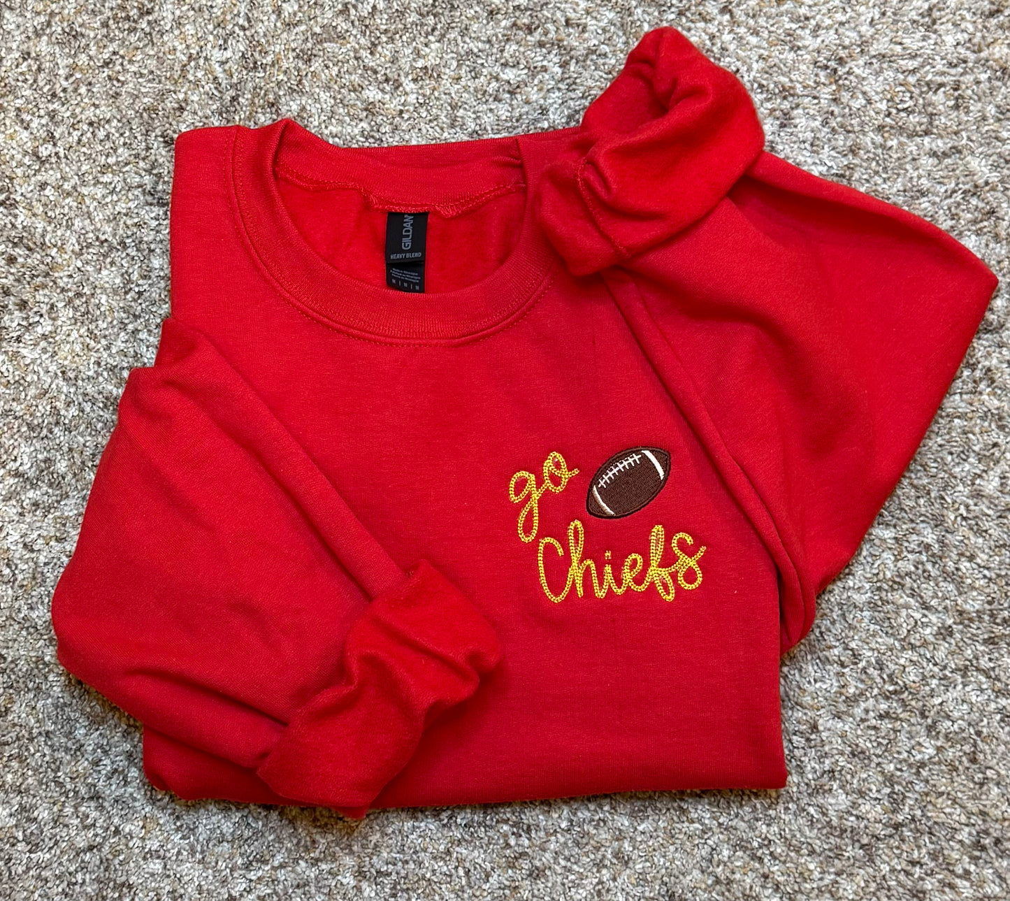 Folded red sweatshirt with 'go Chiefs' and football graphic on a textured surface