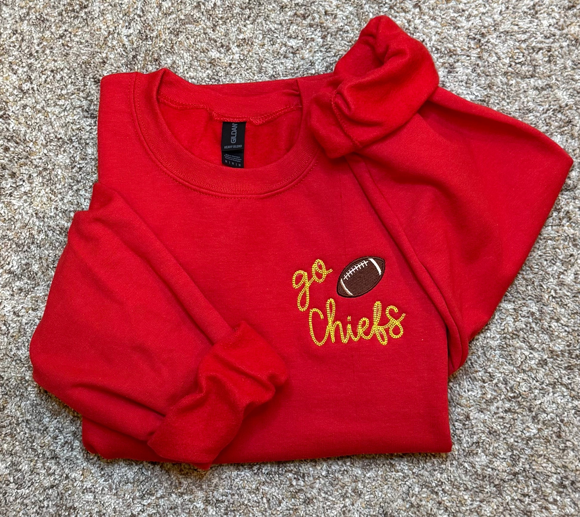 Folded red sweatshirt with 'go Chiefs' and football graphic on a textured surface